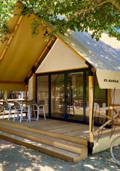 Tenda glamping moderna con veranda in legno e sedie bianche.