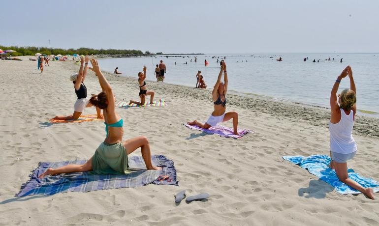 Persone fanno yoga sulla spiaggia di fronte al mare.