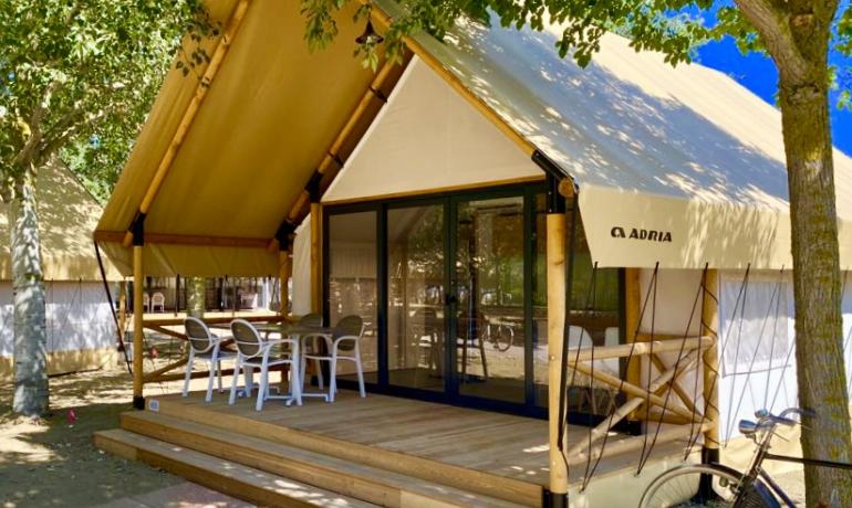 Modern glamping tent with wooden porch and white chairs.