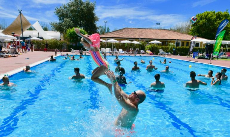 Mand kaster barn i fyldt pool, solrig dag.