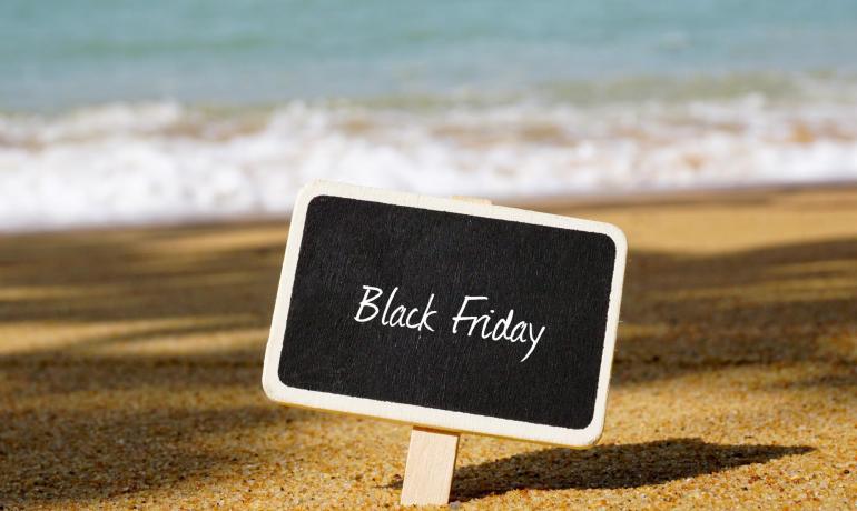 Black Friday Schild am sonnigen Strand mit Meer im Hintergrund.