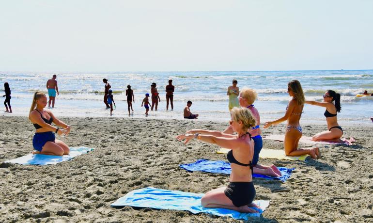Folk laver yoga på stranden med havet i baggrunden.