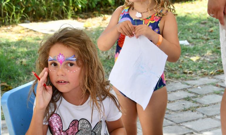 Mädchen zeichnen im Freien mit Gesichtsbemalung und Farben.