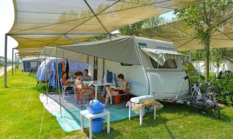 Famiglia in campeggio con roulotte sotto tettoie ombreggianti.