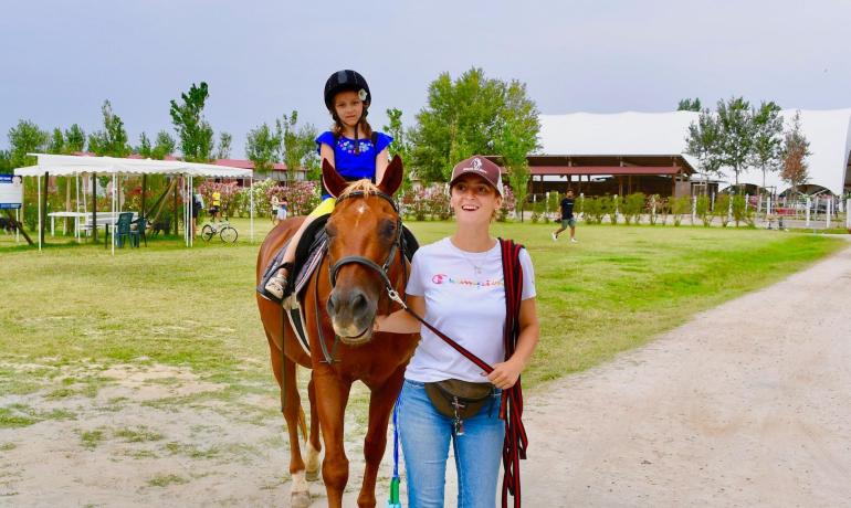 Bambina a cavallo guidata da una donna in un campo.