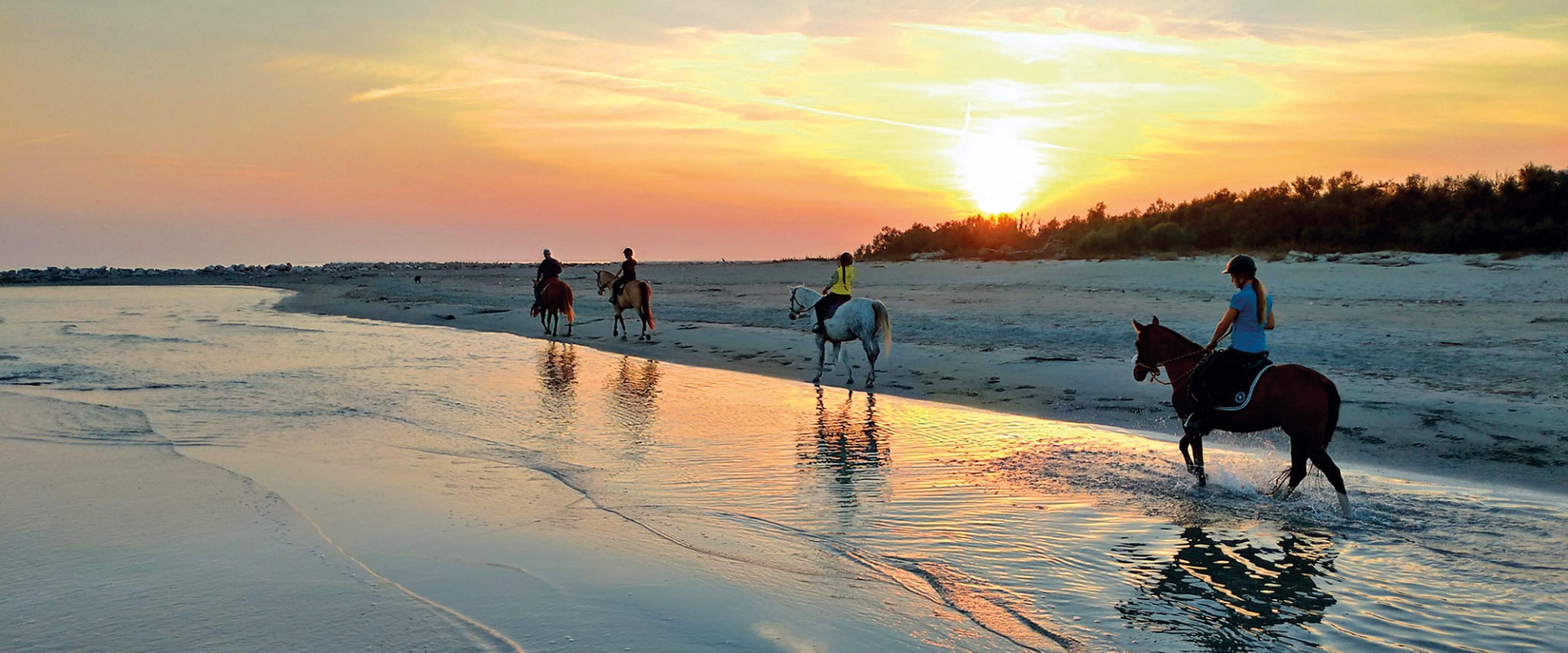 Cavalieri al tramonto sulla spiaggia, riflessi nell'acqua.