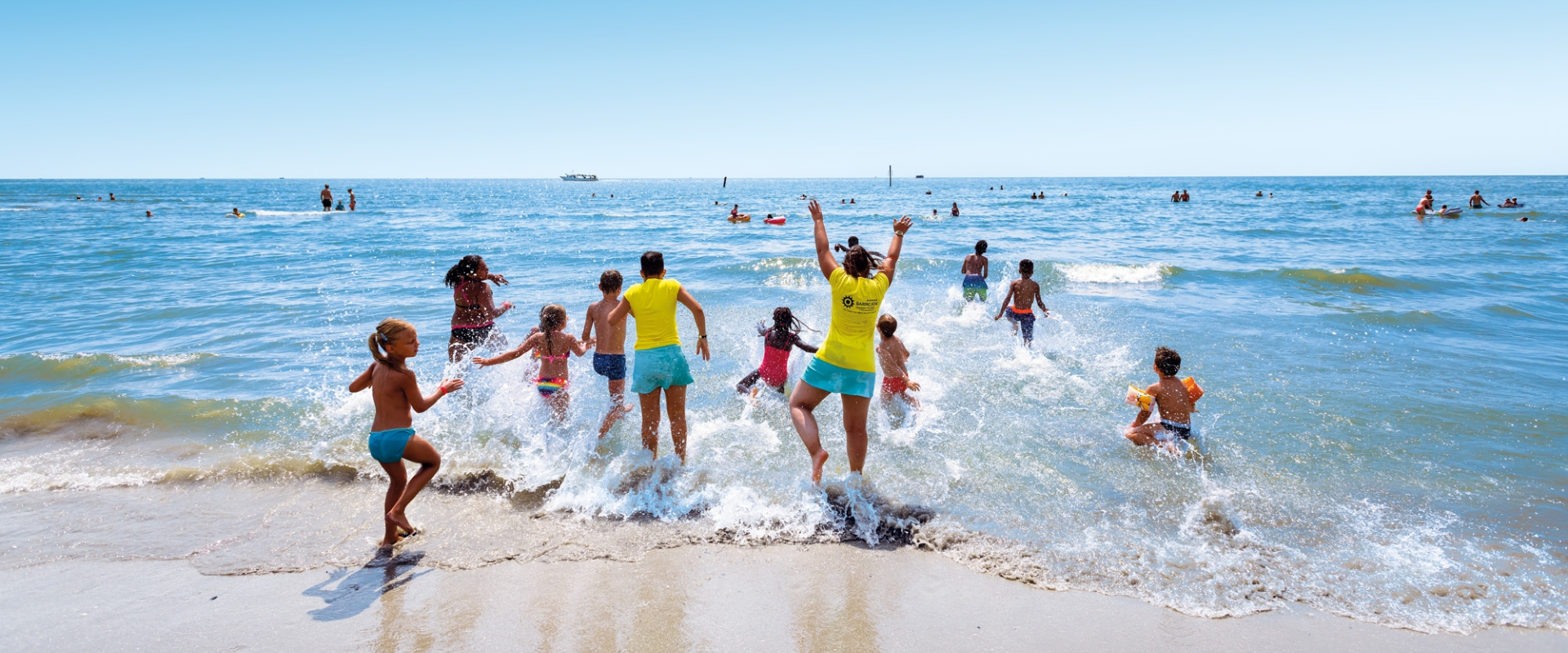 Bambini e adulti corrono felici verso il mare in una giornata estiva.
