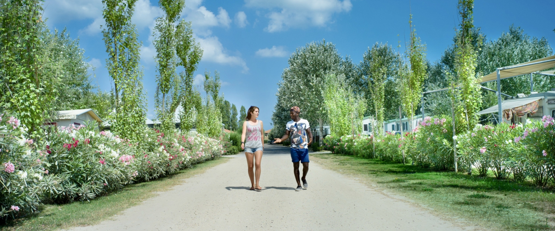To personer går glade på en blomstrende campingplads under en klar himmel.