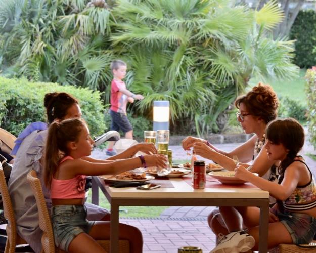Famiglia mangia all'aperto, bambini giocano, ambiente verde e rilassante.