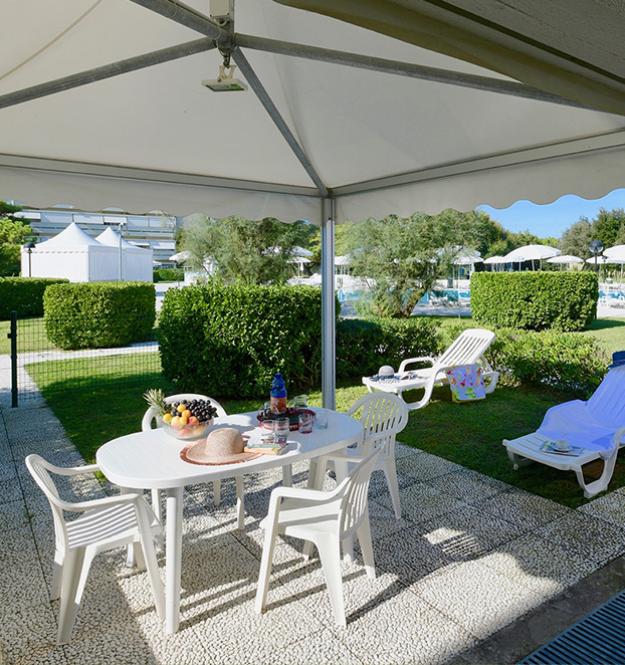 Gazebo con tavolo, sedie, frutta e piscina sullo sfondo.