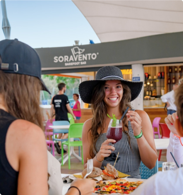Giovani al bar Soravento, sorridono e gustano bevande e cibo all'aperto.