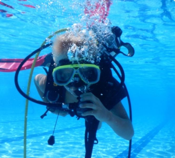 Bambino con attrezzatura subacquea nuota sott'acqua in piscina, creando bolle d'aria.