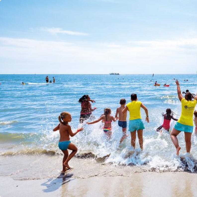 Bambini e adulti corrono felici verso il mare in una giornata soleggiata.