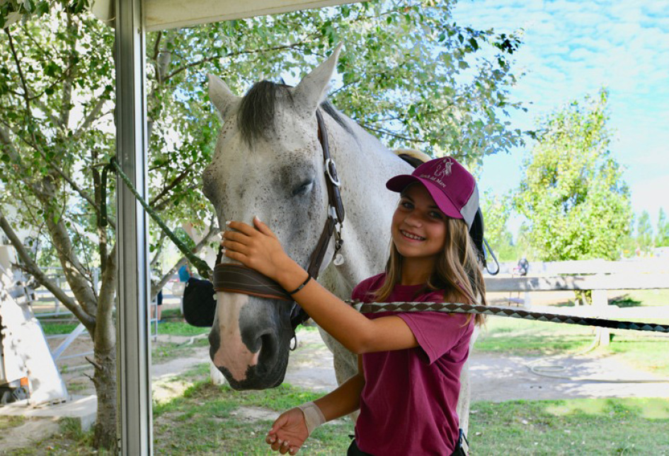 Bambino su pony con istruttrice in un campo aperto, giornata di sole.