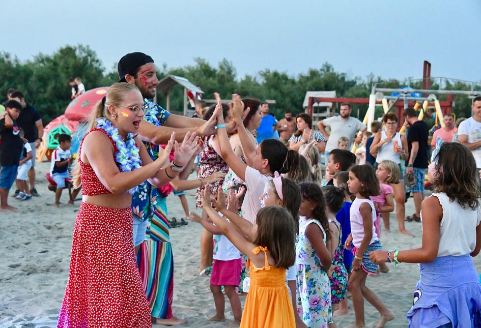 Festa in spiaggia con bambini e animatori che ballano e giocano insieme.