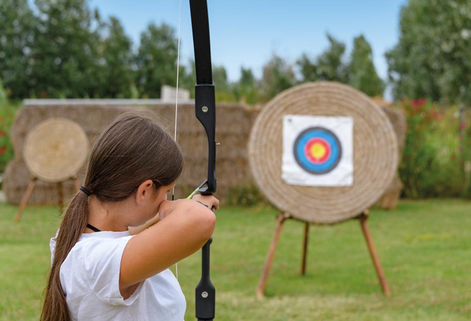 Ragazza pratica tiro con l'arco all'aperto, mirando a bersaglio circolare su paglia.