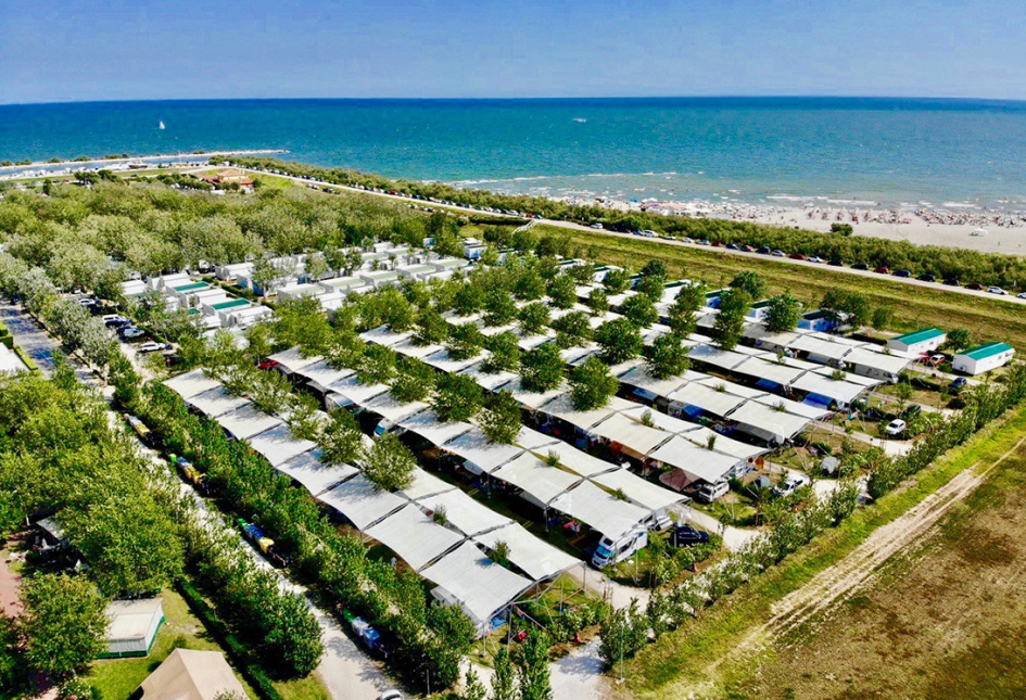Campeggio vicino al mare con roulotte coperte e alberi disposti in file ordinate.