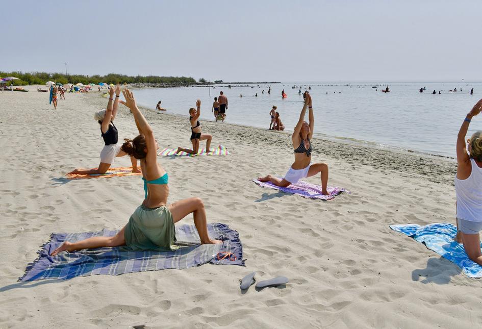 Persone praticano yoga sulla spiaggia, allineate su asciugamani, fronte mare.